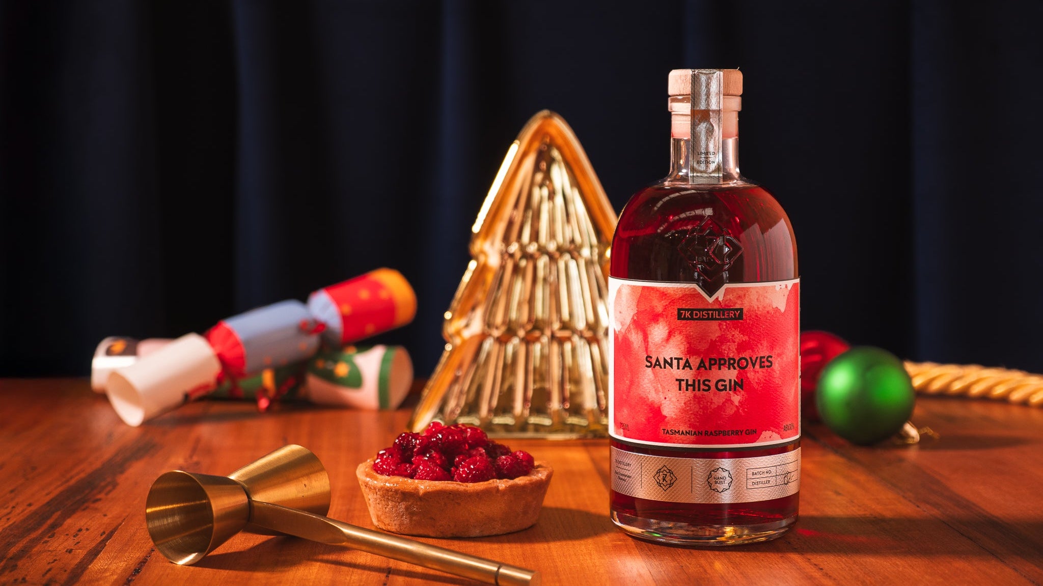Bottle of 'Santa Approves This Gin' on a wooden table with festive decorations.